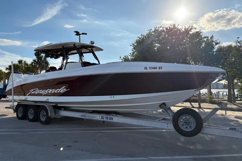 Slide: The Image of 2021 Renegade 33 boat on trailer, parked under sunny sky with trees in background. - 4
