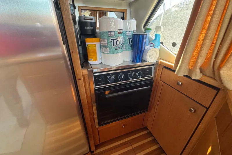 Slide: The Image of 1998 Bayliner 4087 yacht kitchen with stove, cleaning supplies, and wooden cabinetry. - 25