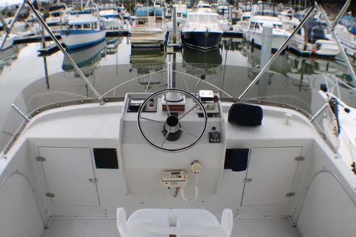 Slide: The Image of 1986 Lynnwood Flybridge Sedan helm with marina view, showcasing steering wheel and controls. - 30