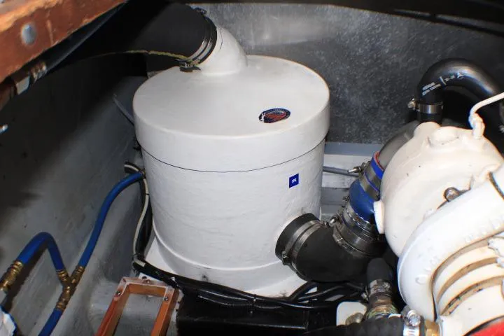 Slide: The Image of Engine room of a 1986 Lynnwood Flybridge Sedan, featuring a white cylindrical component and blue hoses. - 64