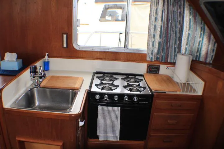 Slide: The Image of 1986 Lynnwood Flybridge Sedan kitchen with stove, sink, and wooden cabinetry. - 77