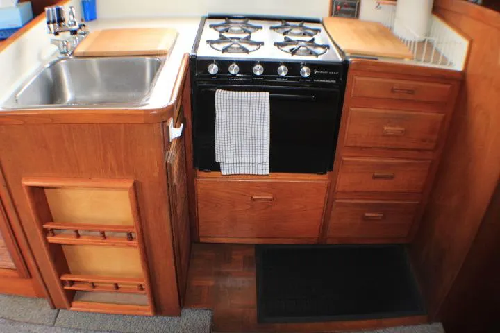 Slide: The Image of 1986 Lynnwood Flybridge Sedan kitchen with stove, sink, and wooden cabinetry. - 78