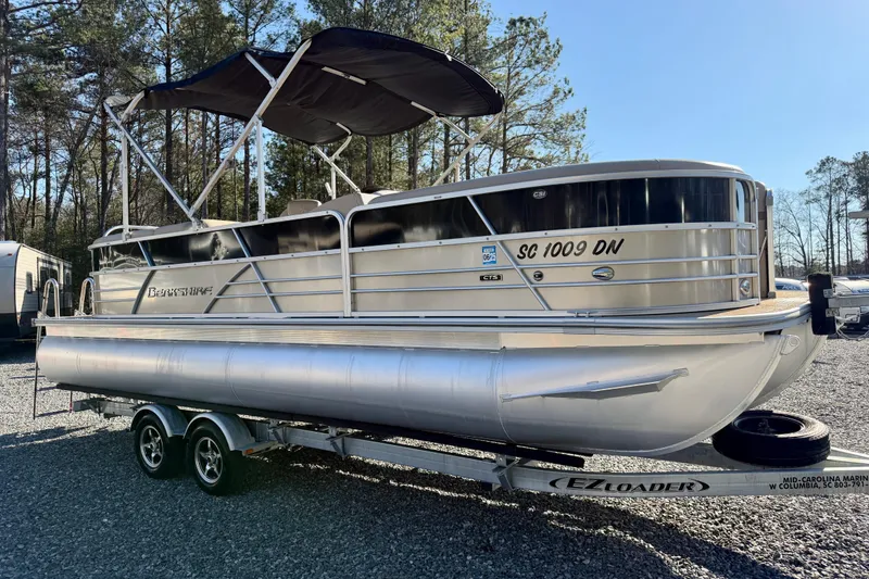 Slide: The Image of 2020 Berkshire 25SL pontoon boat on trailer, parked outdoors with trees in background. - 3