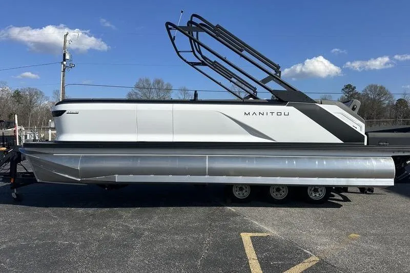 Slide: The Image of 2024 Manitou Cruise 22 Bench Tritoon boat on trailer under clear blue sky. - 5