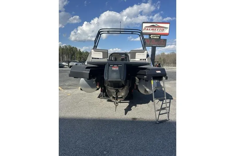 Slide: The Image of 2024 Manitou Cruise 22 Bench Tritoon with outboard motor, parked outdoors. - 6