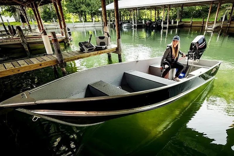 Slide: The Image of Manufacturer Provided Image: 2026 Lund WC-14 boat docked with person seated, surrounded by calm water and wooden piers. - 11