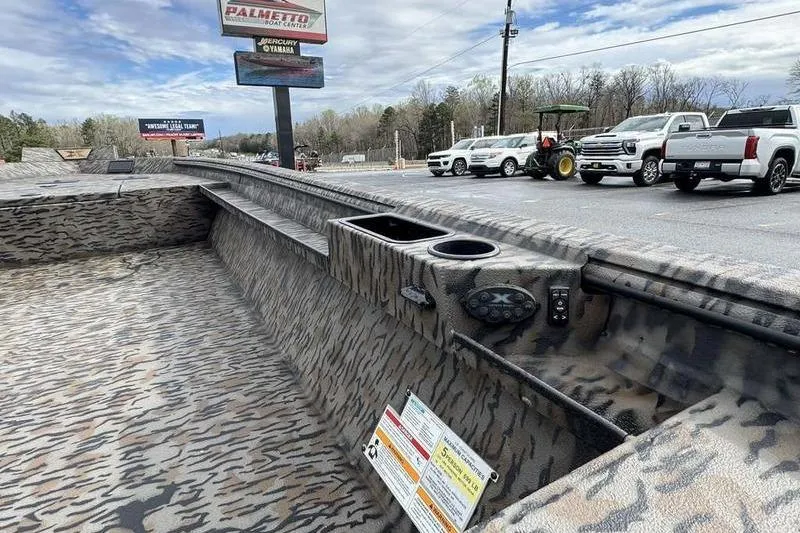 Slide: The Image of 2026 Xpress X18DB boat interior with camouflage design, parked outdoors near vehicles. - 16