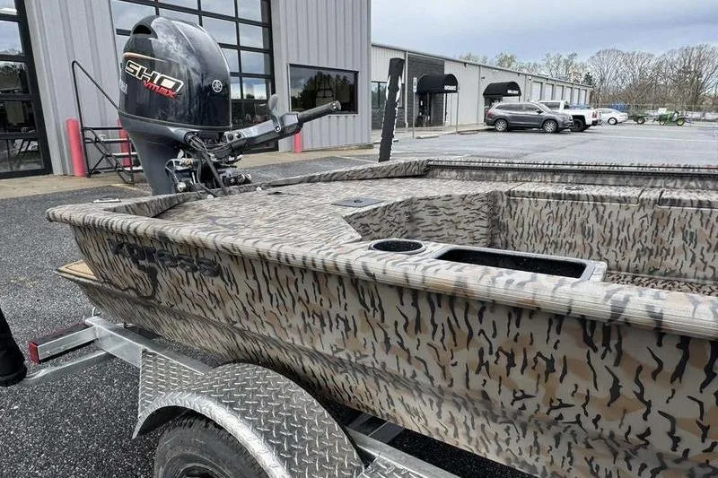 Slide: The Image of 2026 Xpress X18DB boat with camouflage design on a trailer, parked outside a building. - 18