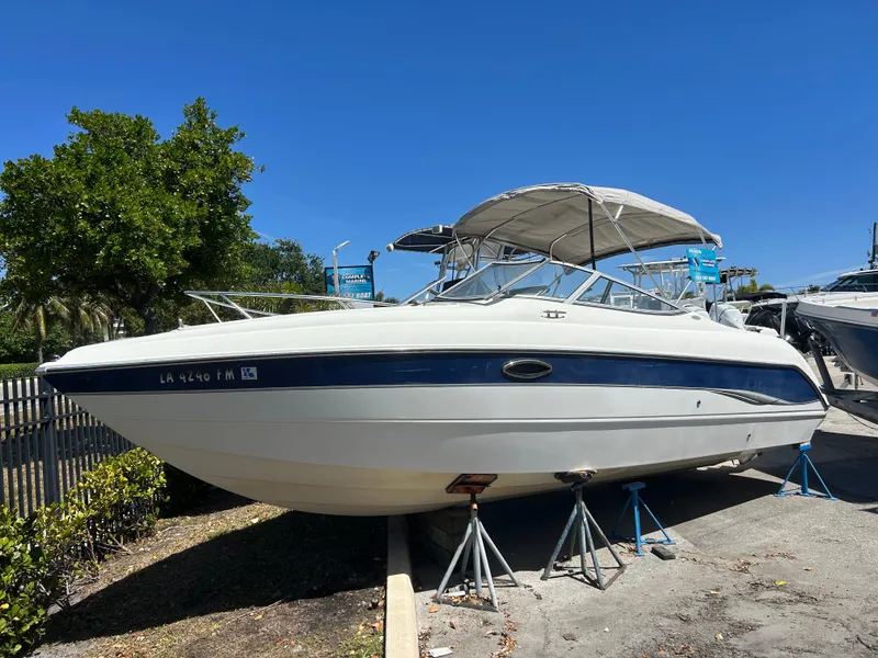 The Image of 2003 Stingray 240 LR boat on stands, white with blue stripe, sunny day. - 0