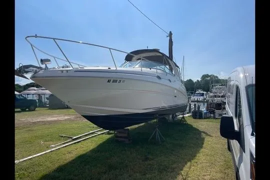 The Image of 2004 Sea Ray Sundancer 280 boat on land, parked beside a van, under clear sky. - 1