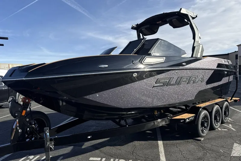 The Image of 2026 Supra SE 550 boat on trailer, sleek black design under clear sky. - 1