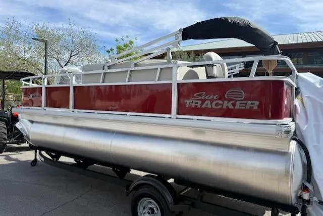 Slide: The Image of 2026 Sun Tracker Bass Buggy 18 DLX pontoon boat on trailer, parked outdoors. - 2