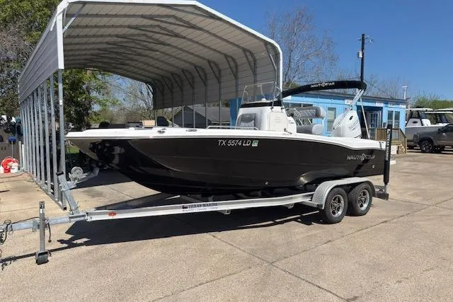 The Image of 2024 NauticStar 211 Hybrid boat on trailer under canopy, parked outdoors. - 1