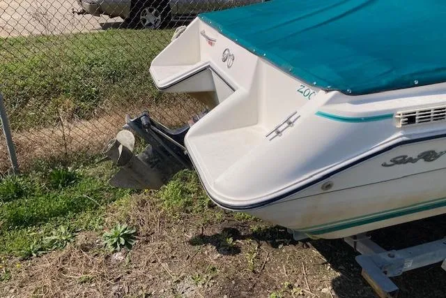 Slide: The Image of 1990 Searay 200 Cuddy boat with teal cover, parked on grass near a fence. - 6