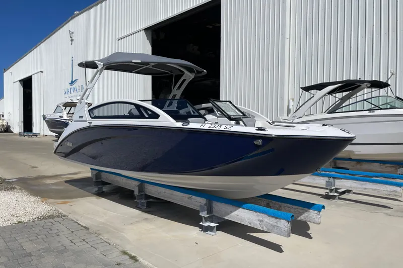 The Image of 2021 Yamaha Boats 275SE in marina, blue and white, docked outside a large warehouse. - 0