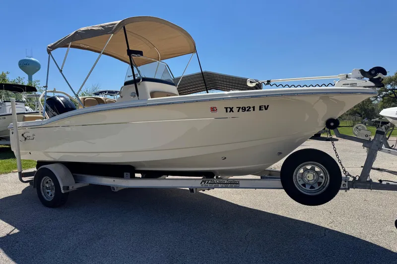 The Image of 2018 Scout 195 Sportfish boat on trailer with canopy, parked outdoors. - 1