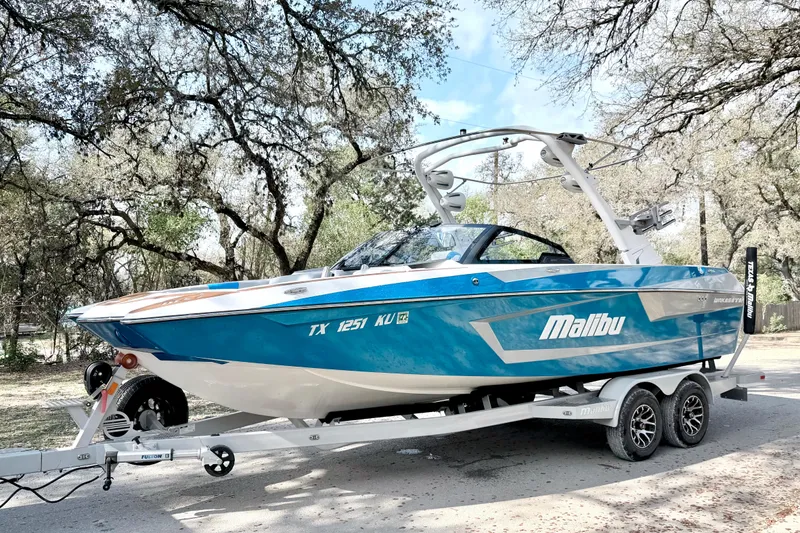 Slide: The Image of 2023 Malibu Wakesetter 23 MXZ boat on trailer, parked outdoors under trees. - 14