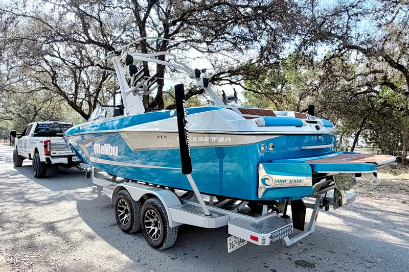 Slide: The Image of 2023 Malibu Wakesetter 23 MXZ boat on trailer, parked under trees. - 16