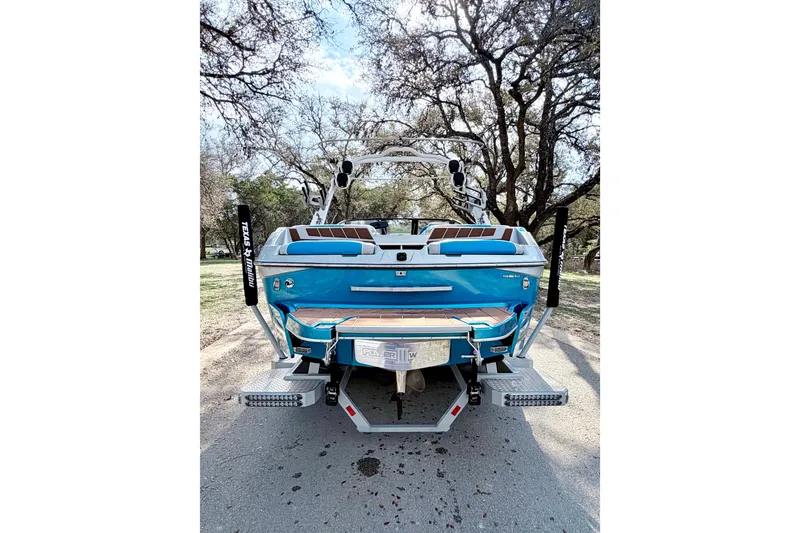 Slide: The Image of 2023 Malibu Wakesetter 23 MXZ boat, blue exterior, parked outdoors with trees in background. - 18