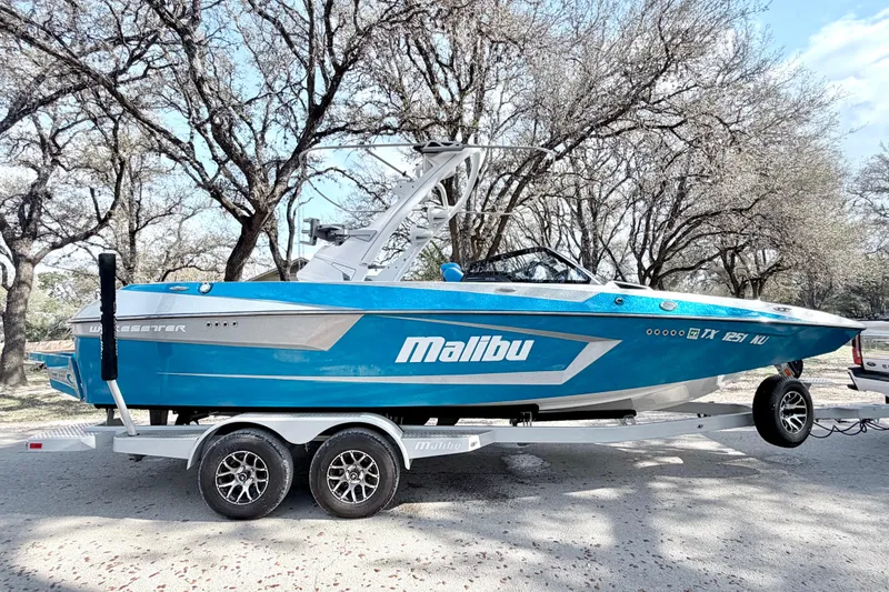 Slide: The Image of 2023 Malibu Wakesetter 23 MXZ boat on trailer, parked outdoors among trees. - 20