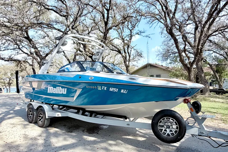 Slide: The Image of 2023 Malibu Wakesetter 23 MXZ boat on trailer, parked under trees. - 21