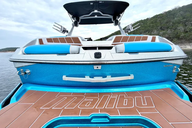 Slide: The Image of 2023 Malibu Wakesetter 23 MXZ boat with blue and brown deck, on a lake. - 24