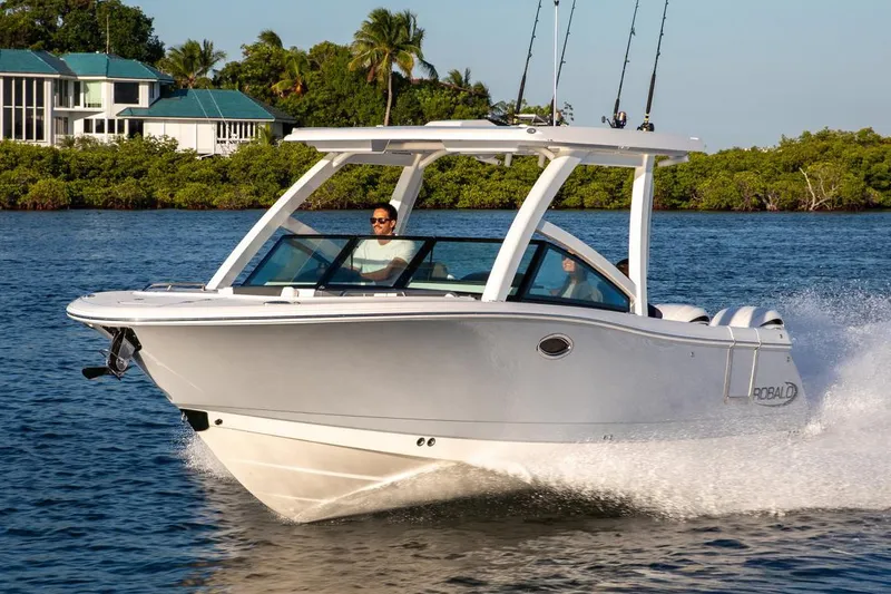 The Image of Manufacturer Provided Image: 2026 Robalo R277 Dual Console boat cruising on a sunny day near lush shoreline. - 0