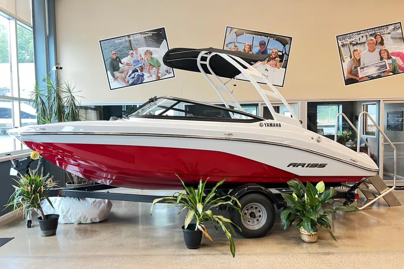 The Image of 2024 Yamaha Boats AR195 in showroom, red and white design, surrounded by plants. - 0