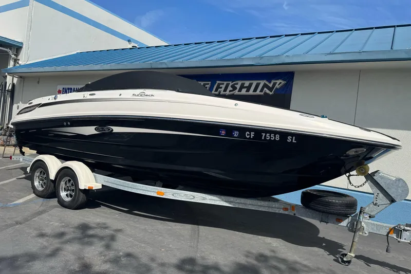 Slide: The Image of 2012 Sea Ray 240 Sundeck boat on trailer, parked outdoors under blue sky. - 3