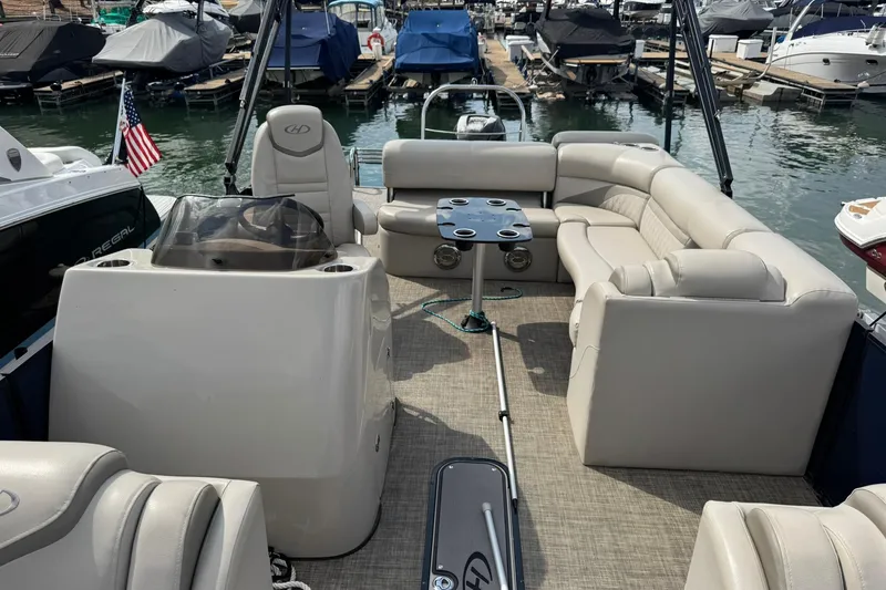 Slide: The Image of 2017 Harris FloteBote 240 Sunliner pontoon boat interior at marina, featuring plush seating and table. - 6