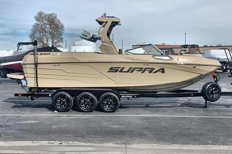 Slide: The Image of 2026 Supra SE 550 boat on trailer, beige color, parked outdoors. - 8