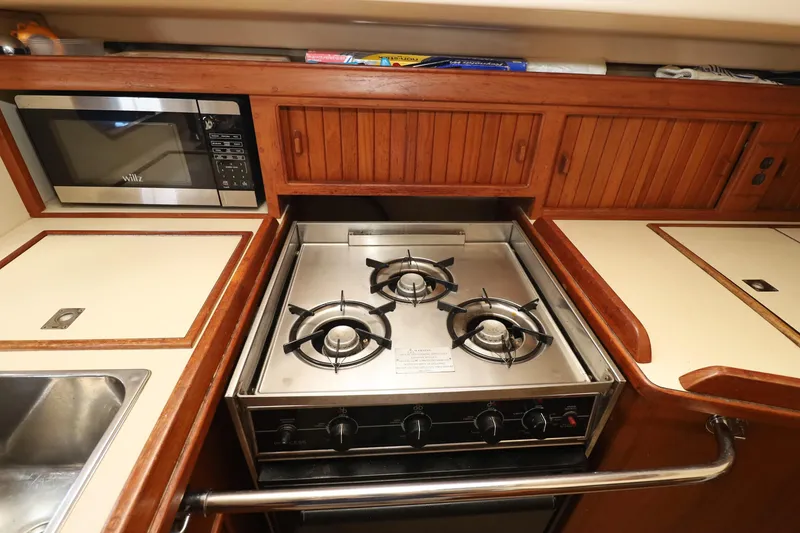 Slide: The Image of 1996 Island Packet 40 yacht kitchen with stove, microwave, and wooden cabinetry. - 11
