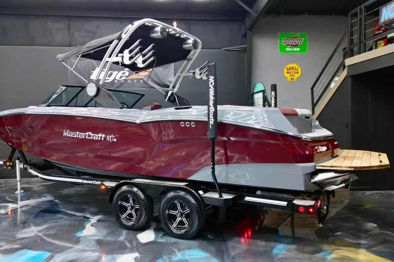 The Image of 2023 MasterCraft NXT24 boat on trailer in showroom, featuring sleek design and vibrant colors. - 0