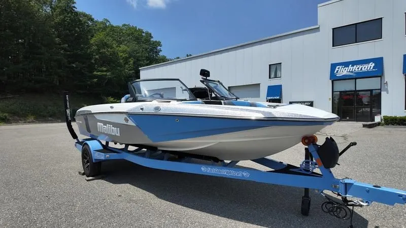 The Image of 2025 Malibu TXi boat on trailer in front of building. - 1