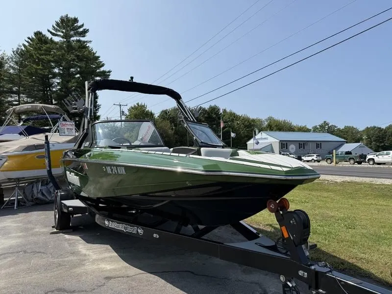 Slide: The Image of Green 2022 Malibu TXi boat on trailer, parked outdoors. - 13