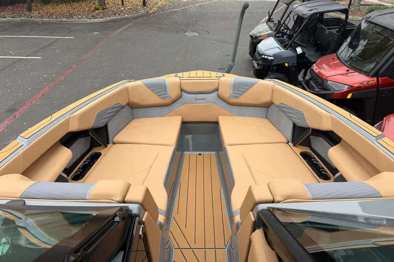 Slide: The Image of 2026 MasterCraft X24 boat interior with tan and gray seating, parked outdoors. - 57