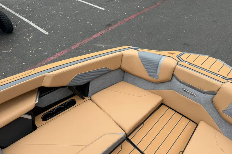 Slide: The Image of 2026 MasterCraft X24 boat interior with tan and gray seating, parked on asphalt. - 64