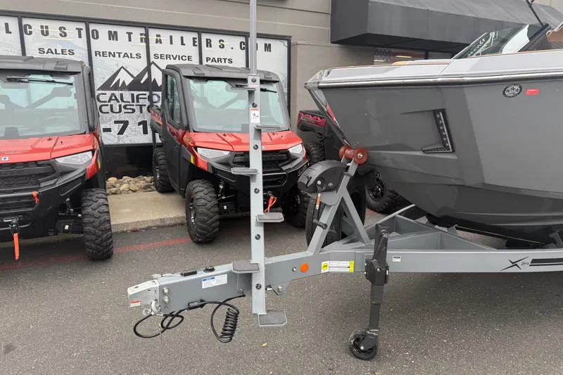 Slide: The Image of 2026 MasterCraft X24 boat on trailer beside two red ATVs at dealership. - 8