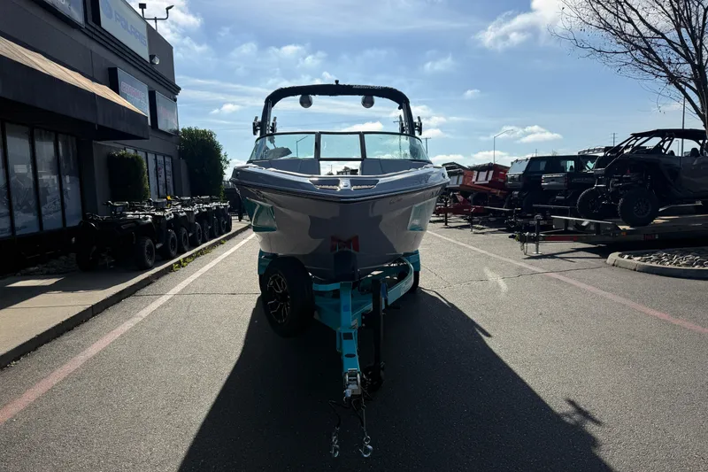 Slide: The Image of 2026 MasterCraft XT23 boat on trailer in dealership parking lot under blue sky. - 6