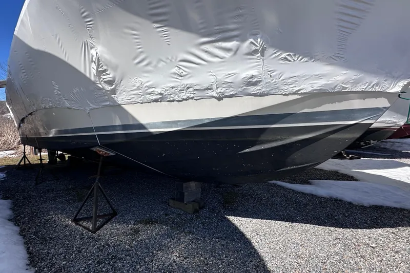 Slide: The Image of 1988 Silverton 37 Convertible boat covered and stored on gravel with snow patches. - 5