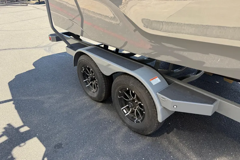 Slide: The Image of 2025 MasterCraft XT22 boat trailer with dual black wheels on asphalt. - 10