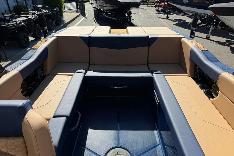 Slide: The Image of 2026 MasterCraft NXT23 boat interior with tan and blue seating, parked outdoors. - 18