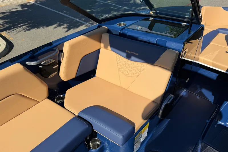 Slide: The Image of 2026 MasterCraft NXT23 boat interior with tan and blue seating, cup holders, and sleek design. - 22