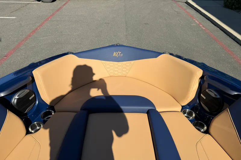 Slide: The Image of 2026 MasterCraft NXT23 boat interior with tan and blue seating, cup holders, and speaker system. - 26
