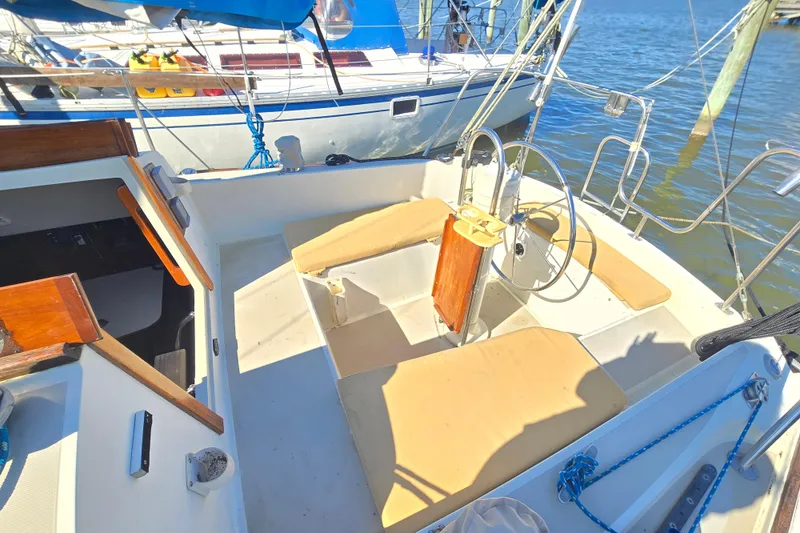 Slide: The Image of 1985 O'Day 31 sailboat cockpit with steering wheel and beige seating, docked by the water. - 32
