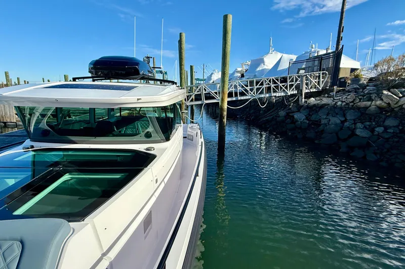 Slide: The Image of 2023 Axopar 37 Cross Cabin boat docked in a marina under clear blue skies. - 14