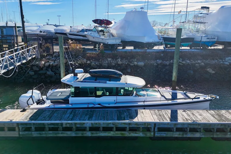 Slide: The Image of 2023 Axopar 37 Cross Cabin boat docked at a marina, surrounded by other vessels. - 2