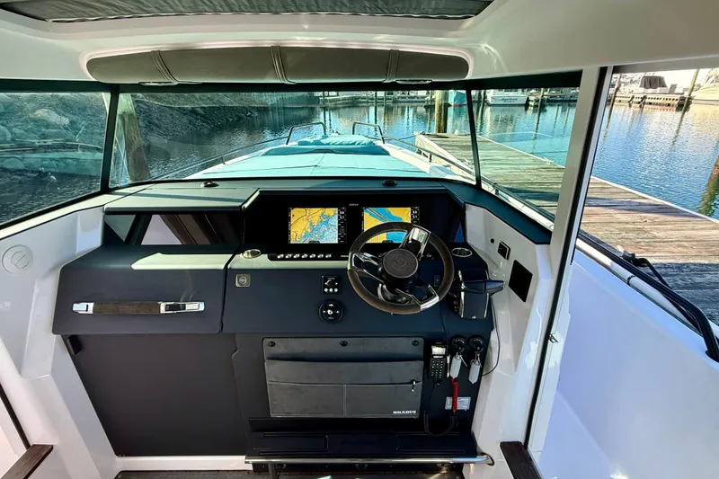 Slide: The Image of 2023 Axopar 37 Cross Cabin helm with navigation display, steering wheel, and dock view. - 34