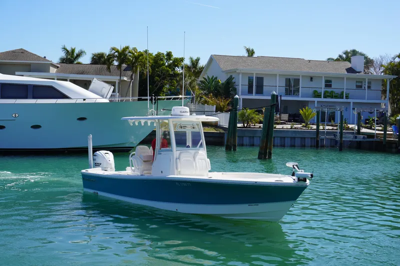 Slide: The Image of 2024 Regulator 26XO boat cruising in a sunny waterfront setting with houses and yachts. - 9