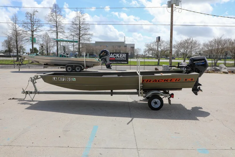 Slide: The Image of 2025 Tracker Grizzly 1436 Jon boat on trailer, parked outdoors under a cloudy sky. - 2